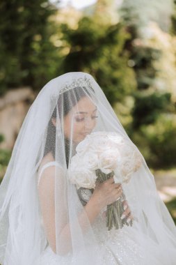 İnanılmaz güzel elbiseli güzel bir gelin buketten zevk alır ve onu koklar. Yaz düğünü. Lüks bir gelin..