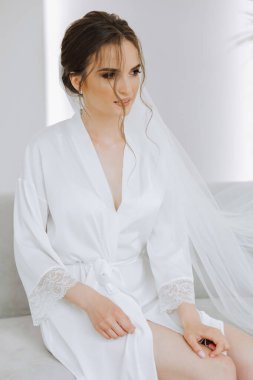 Düğün töreninden önce sabahları sabahlık giymiş güzel bir gelin. Gelinin saç stili inanılmaz. Doğal ve modern makyaj. Sabahlık giymiş genç bir gelinin portresi.