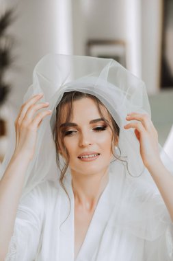 Düğün töreninden önce sabahları sabahlık giymiş güzel bir gelin. Gelinin saç stili inanılmaz. Doğal ve modern makyaj. Sabahlık giymiş genç bir gelinin portresi.