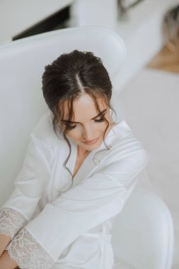 Düğün töreninden önce sabahları sabahlık giymiş güzel bir gelin. Gelinin saç stili inanılmaz. Doğal ve modern makyaj. Sabahlık giymiş genç bir gelinin portresi.