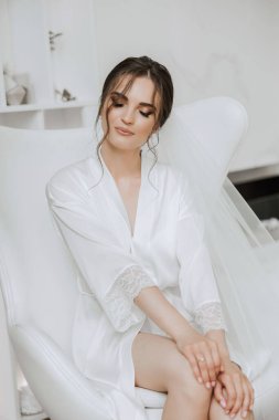 Güzel bir gelin sabahleyin modern bir iç mimarisi olan bir otelde düğün töreninden önce sabahlıkla oturuyor. Gelinin saç stili inanılmaz. Doğal ve modern makyaj..