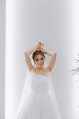 Otel odasında gelinin portresi. Güzel genç bir kız beyaz bir gelinlik giyiyor. Modern düğün saç stili. Doğal makyaj..