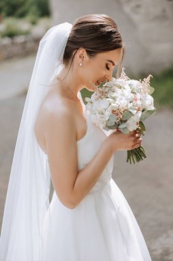 İnanılmaz güzel elbiseli güzel bir gelin buketten zevk alır ve onu koklar. Yaz düğünü. Lüks bir gelin..