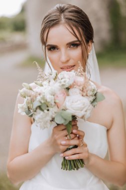 İnanılmaz güzel elbiseli güzel bir gelin buketten zevk alır ve onu koklar. Yaz düğünü. Lüks bir gelin..