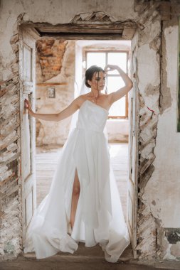 Uzun duvağı ve güzel saç stili olan beyaz elbiseli güzel bir gelinin portresi. Gülümseyen bir gelin yıkılmış duvarları olan bir stüdyo odasında duruyor..