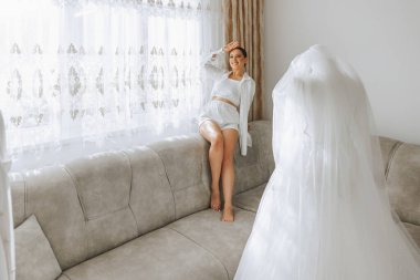 Odasında uzun peçeli, bornoz giymiş güzel bir gelin. Bir mankenin üzerinde gelinlik. Düğün töreninden önceki sabah gelin..