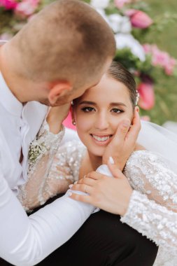 Damat, bir yaz günü gelinini tapınakta güzel bir doğanın arka planına karşı öper. - Sanat. Seçici odak.