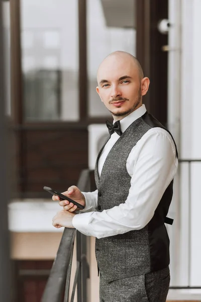 a young man in a classic suit stands on a balcony with a phone in his hand. High quality vertical photo.