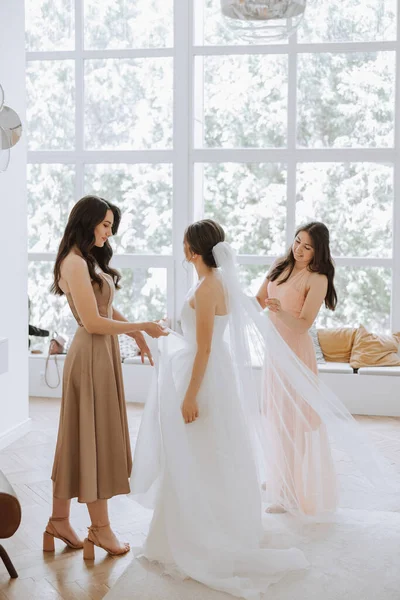 結婚式の朝だった 花嫁は白いウェディングドレスを着るのに役立ちます 若い女性は彼女の成長に会い 彼女の友人と楽しむ準備をしている — ストック写真