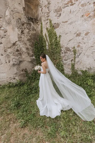 背中からの写真 白いウェディングドレスの美しい若い女性が暖かい結婚式の夏の日に微笑んでいる — ストック写真