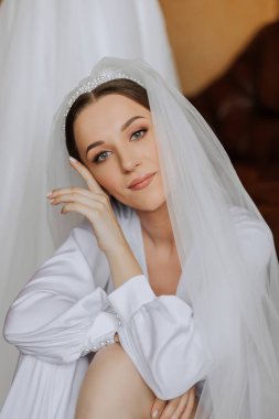 Düğün töreninden önce sabahları sabahlık giymiş güzel bir gelin. Gelinin saç stili inanılmaz. Doğal ve modern makyaj. Sabahlık giymiş genç bir gelinin portresi.