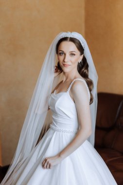 Otel odasında gelinin portresi. Güzel genç bir kız beyaz bir gelinlik giyiyor. Modern düğün saç stili. Doğal makyaj..