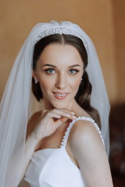 Otel odasında gelinin portresi. Güzel genç bir kız beyaz bir gelinlik giyiyor. Modern düğün saç stili. Doğal makyaj..