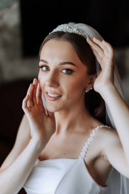 Otel odasında gelinin portresi. Güzel genç bir kız beyaz bir gelinlik giyiyor. Modern düğün saç stili. Doğal makyaj..