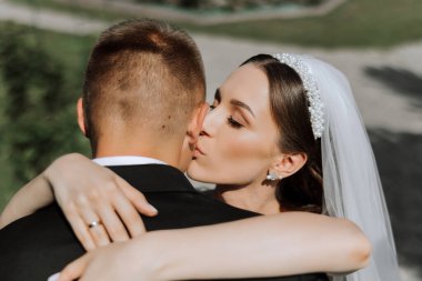 Gelin ve damat öpüşüyor. Düğün buketi olan yeni evliler, açık hava çiçekleriyle süslenmiş kemerin altında düğün töreninde duruyorlar..