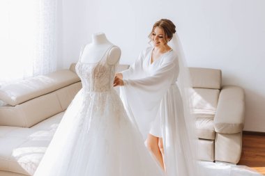 Odasında uzun peçeli, bornoz giymiş güzel bir gelin. Bir mankenin üzerinde gelinlik. Düğün töreninden önceki sabah gelin..