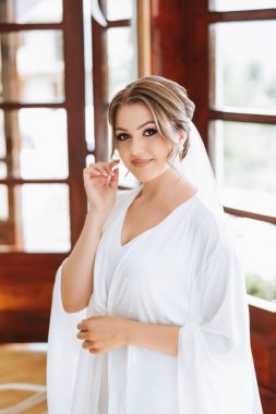 Düğün töreninden önce sabahları sabahlık giymiş güzel bir gelin. Gelinin saç stili inanılmaz. Doğal ve modern makyaj. Sabahlık giymiş genç bir gelinin portresi.