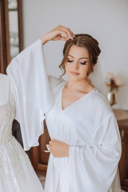 Düğün töreninden önce sabahları sabahlık giymiş güzel bir gelin. Gelinin saç stili inanılmaz. Doğal ve modern makyaj. Sabahlık giymiş genç bir gelinin portresi.