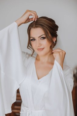 Düğün töreninden önce sabahları sabahlık giymiş güzel bir gelin. Gelinin saç stili inanılmaz. Doğal ve modern makyaj. Sabahlık giymiş genç bir gelinin portresi.