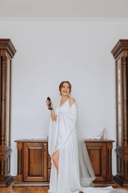 Genç ve güzel bir gelin kız elinde zarif bir parfüm şişesi tutuyor ve kendini spreylemeye hazır. Düğün töreninden önce gelinin sabahı.