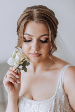 Otel odasında gelinin portresi. Güzel genç bir kız beyaz bir gelinlik giyiyor. Modern düğün saç stili. Doğal makyaj..