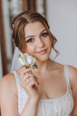 Otel odasında gelinin portresi. Güzel genç bir kız beyaz bir gelinlik giyiyor. Modern düğün saç stili. Doğal makyaj..