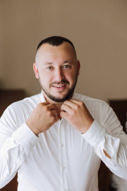 İş gömleği. Beyaz gömlekli bir adam düğmeleri bağlar. Genç politikacı, erkek tarzı, işadamı gömleği, erkek eli yakın, Amerikalı, Avrupalı işadamı