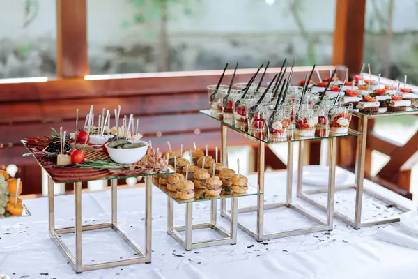 open-air buffet table, sandwiches on skewers before the start of the holiday against the background of flowering trees in the garden