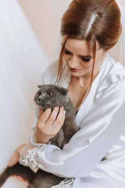 Portrait of a bride in a hotel room with a cat in her hands. A beautiful young girl wearing a white wedding dress. Modern wedding hairstyle. Natural makeup.