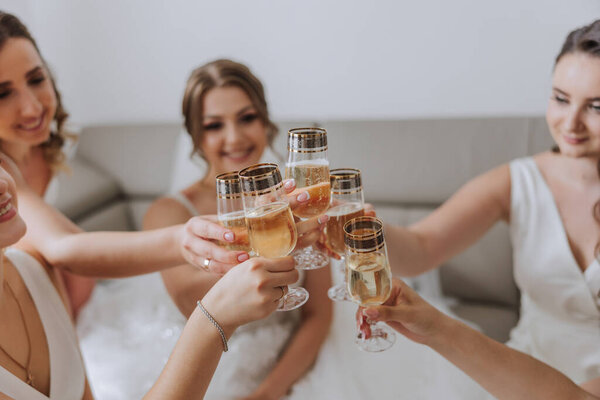 Photo bride with her friends drinking champagne from glasses. Cropped shot of a beautiful young bride and her bridesmaids having champagne before the wedding.