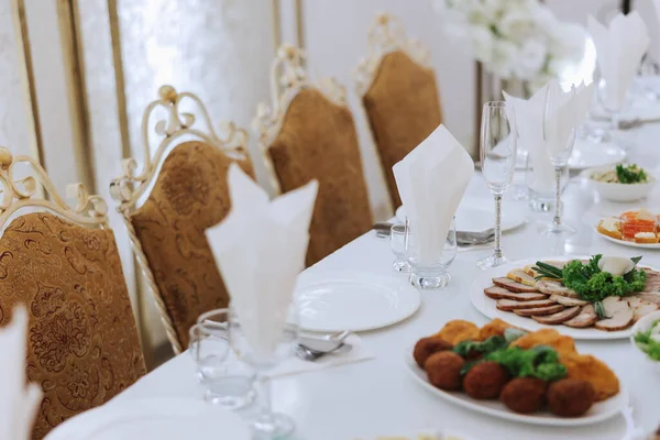A view of wedding tables, attention to serving, with flower arrangements, expensive cutlery, plates with white napkins.
