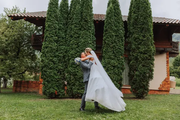 the groom lifted the bride in his arms and is circling in a beautiful garden. Bride and groom dancing in the backyard.