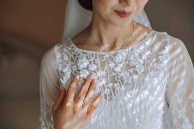 Otel odasında gelinin portresi. Güzel genç bir kız beyaz bir gelinlik giyiyor. Modern düğün saç stili. Doğal makyaj..