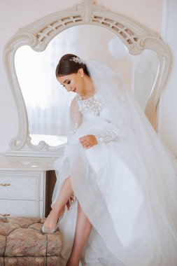 Güzel gelinlikli genç gelin içeride ayakkabı giyiyor. Gelin düğün töreninden önce ayakkabı giyer. Gelinin yüksek topuklu düğün ayakkabısı giymesinin ayrıntıları. Gelin ayakkabıları..