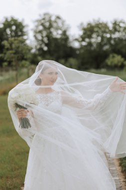 Uzun peçeli ve muhteşem saç stili olan beyaz elbiseli güzel bir gelinin portresi. Gülümseyen gelin. Düğün günü. Harika bir gelin. Evlilik..