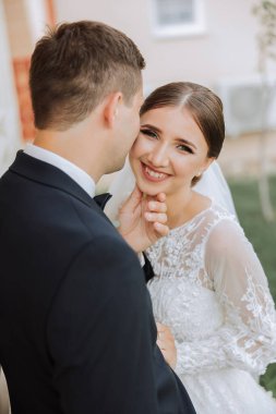 Damat, bir yaz günü gelinini tapınakta güzel bir doğanın arka planına karşı öper. - Sanat. Seçici odak.