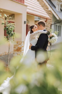 Gelin ve damat kucaklaşır. Gelin damadı nazikçe omuzlarından kucaklıyor. Güzel bir düğün çifti. Yeni evlilerin ilişkilerinde romantizm kavramı. Balayı.
