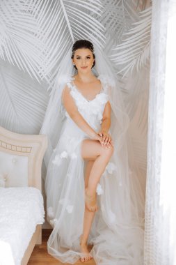 Düğün töreninden önce sabahları sabahlık giymiş güzel bir gelin. Gelinin saç stili inanılmaz. Doğal ve modern makyaj. Sabahlık giymiş genç bir gelinin portresi.