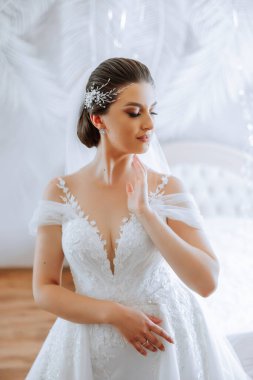 Otel odasında gelinin portresi. Güzel genç bir kız beyaz bir gelinlik giyiyor. Modern düğün saç stili. Doğal makyaj..