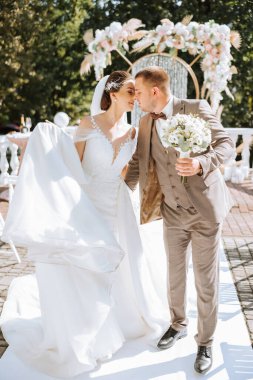 Gelin ve damat düğün kemerinin arka planında yürüyorlar. Açık havada düğün töreni. Damat ve gelin düğün kemerinin arkasında..