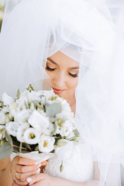 İnanılmaz güzel elbiseli güzel bir gelin buketten zevk alır ve onu koklar. Yaz düğünü. Lüks bir gelin..