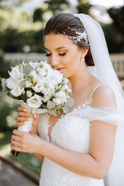 İnanılmaz güzel elbiseli güzel bir gelin buketten zevk alır ve onu koklar. Yaz düğünü. Lüks bir gelin..