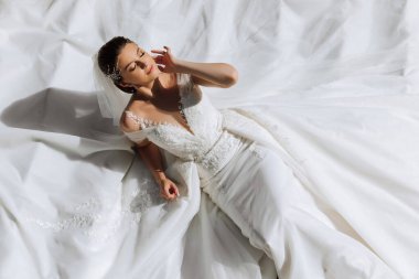 Beyaz elbiseli güzel bir gelin yalan söylüyor. Beyaz elbiseli bir kız dinleniyor. Güzel saç ve makyaj. Manken fotoğrafçı için poz veriyor..