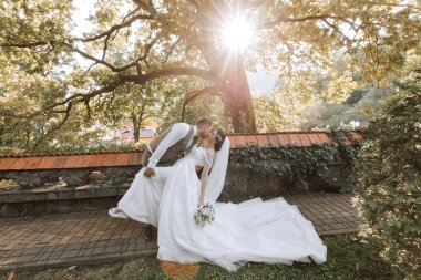 Damat, gelini ateşli bir şekilde öper. Sıcak bir yaz gününde, doğanın arka planında dans eder gibi eğilir..