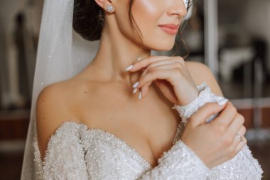 Otel odasında gelinin portresi. Güzel genç bir kız beyaz bir gelinlik giyiyor. Modern düğün saç stili. Doğal makyaj..