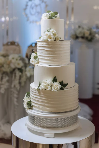 a three-tiered wedding cake decorated with flowers stands on a decorative stand. Decorative wedding cake. Beauty is in the details.