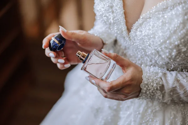 Pink perfume bottle in tender female hands. The bride sprays perfume on her body. Close-up photo. Manicure. Morning of the bride.