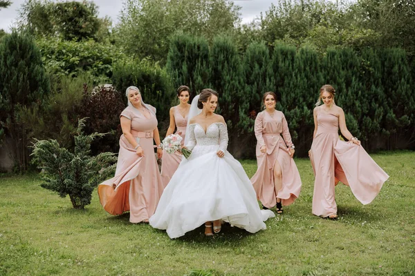一位黑发新娘和她的伴娘穿着相同的粉色衣服 在大自然的背景下行走 穿着相同衣服的女孩在婚礼上亲热 自然结婚 — 图库照片