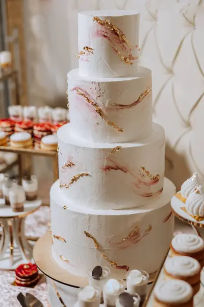 a four-tiered white wedding cake stands on a decorative stand. Decorative wedding cake. Beauty is in the details.