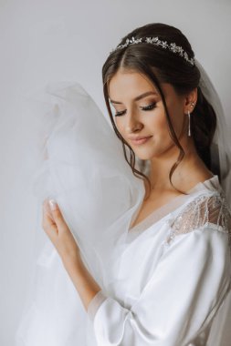 Düğün töreninden önce sabahları sabahlık giymiş güzel bir gelin. Gelinin saç stili inanılmaz. Doğal ve modern makyaj. Sabahlık giymiş genç bir gelinin portresi.